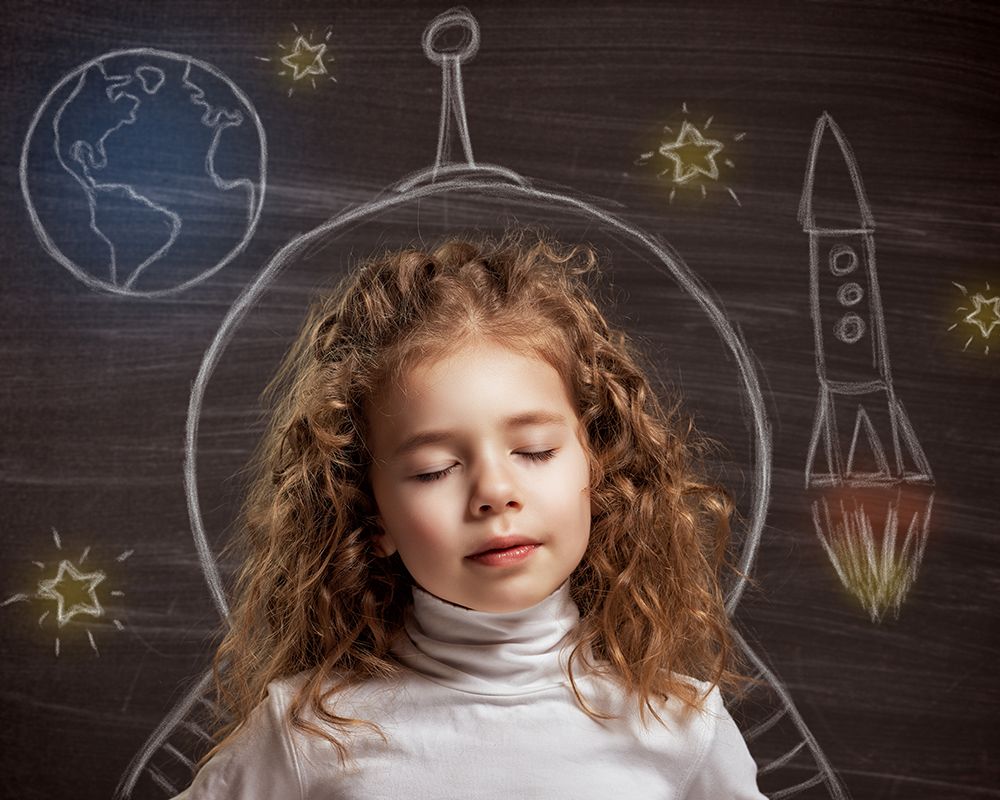 Niña soñando; aparece un dibujo de un cohete, estrellas y el planeta tierra.